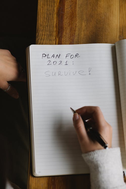 Crop woman writing plans in diary sitting at table