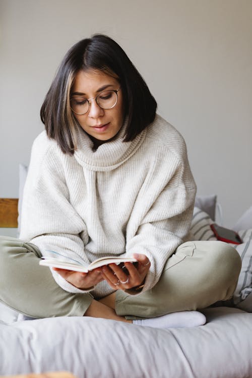 Free Calm young woman resting on sofa and reading novel Stock Photo
