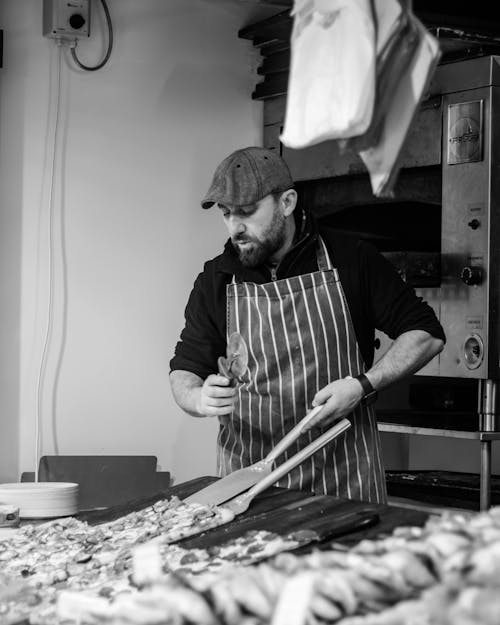 A Grayscale Photo of a Bearded Man Holding a Pizza Cutter