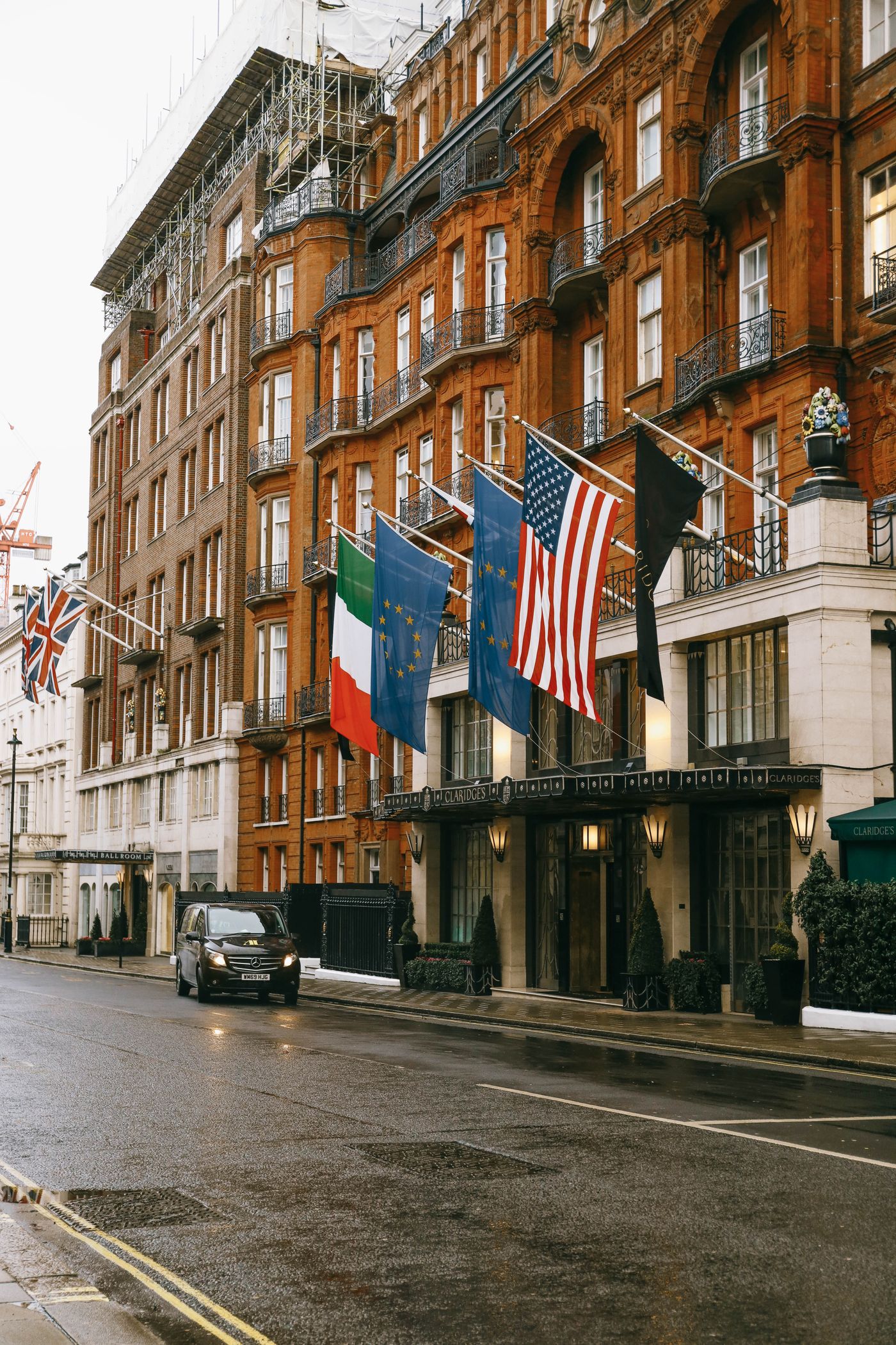 A black van and flags outside Claridge's hotel on a wet street in London