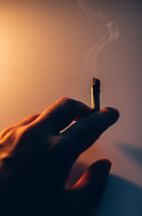 Free A moody vertical shot of a hand holding a smoking cigarette butt against a dark backdrop. Stock Photo