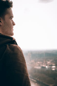 A contemplative man in a brown jacket gazes over the London skyline, captured in a side view.