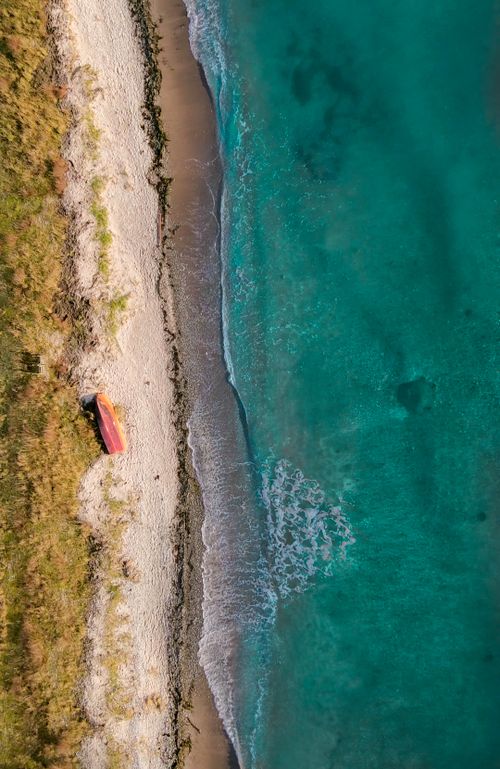 Free Drone shot of a serene beach with turquoise water and a small red boat on the shore. Stock Photo