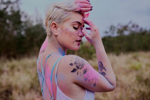 Free Side view of young crop female with tattooes and short fair hair on blurred background of green bushes and meadow Stock Photo