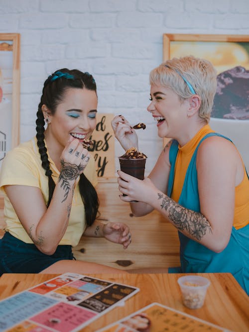Cheerful women with tattoos eating sweet chocolate desserts in cafe
