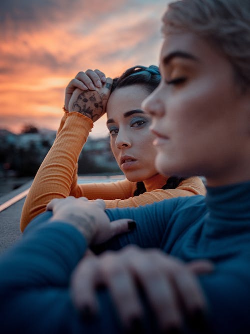 Free Crop young female closing eyes while friend with tattooed hand looking at camera under shiny cloudy sky Stock Photo
