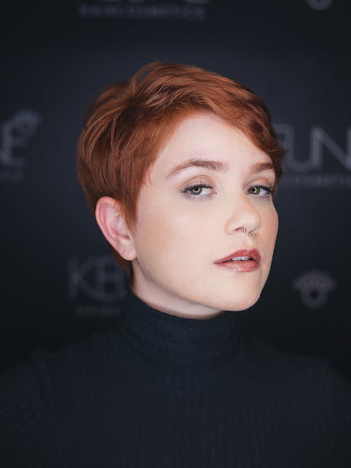 Young ginger female with stylish short haircut and piercing looking at camera on blurred background