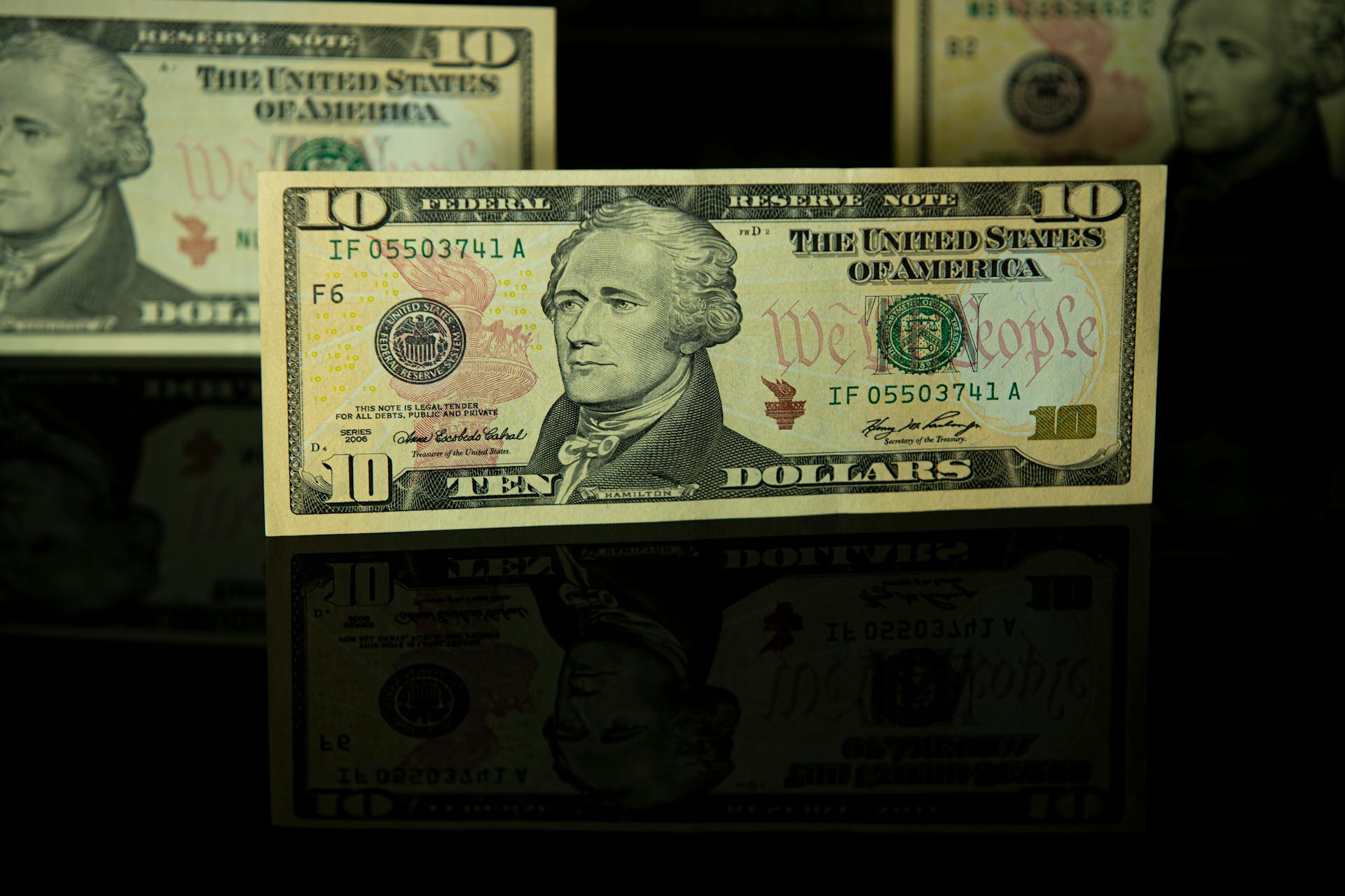 Detailed image of a ten dollar bill with dark reflective background.