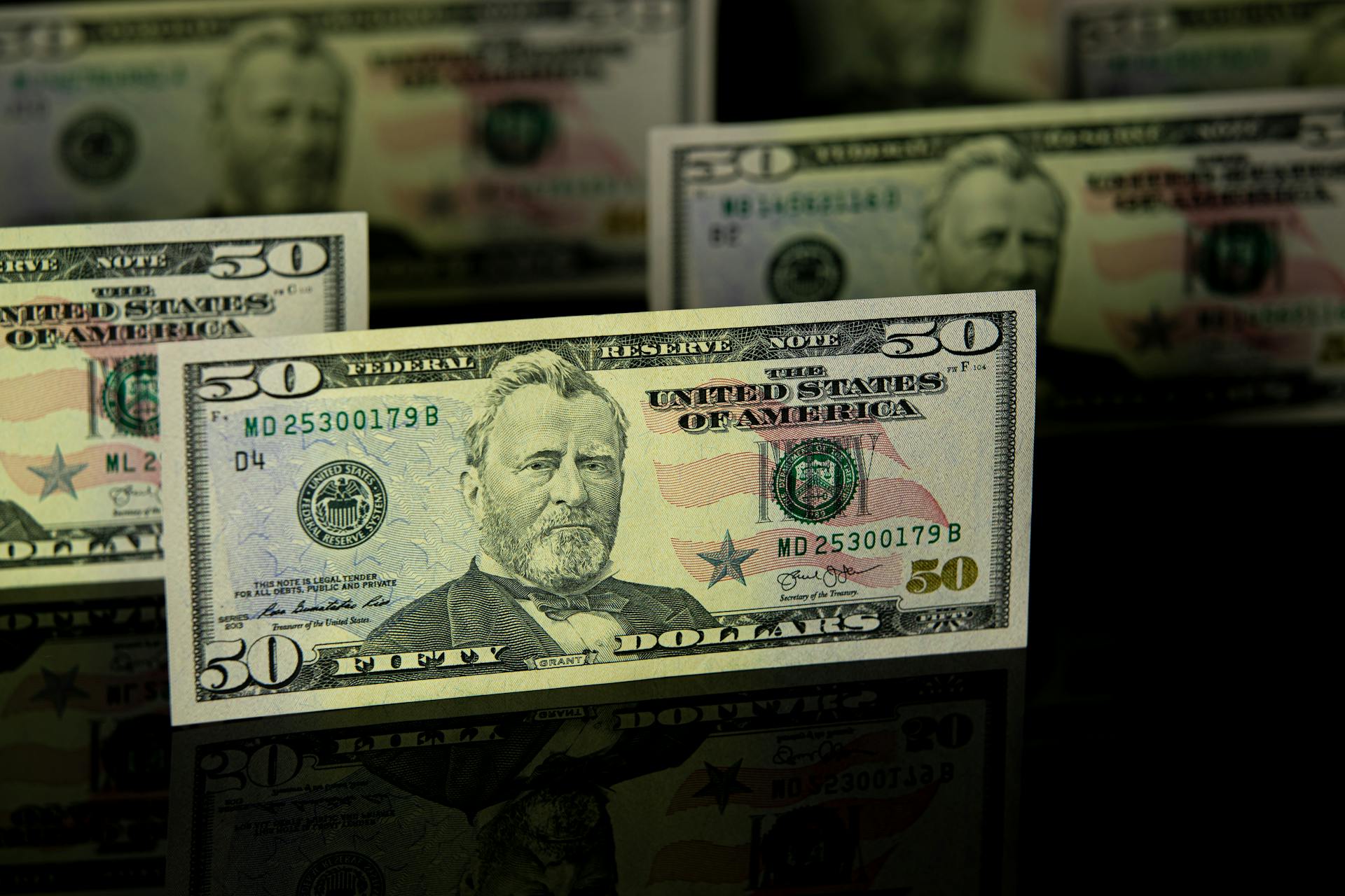 Focused shot of fifty dollar bills on a dark reflective surface, highlighting wealth.