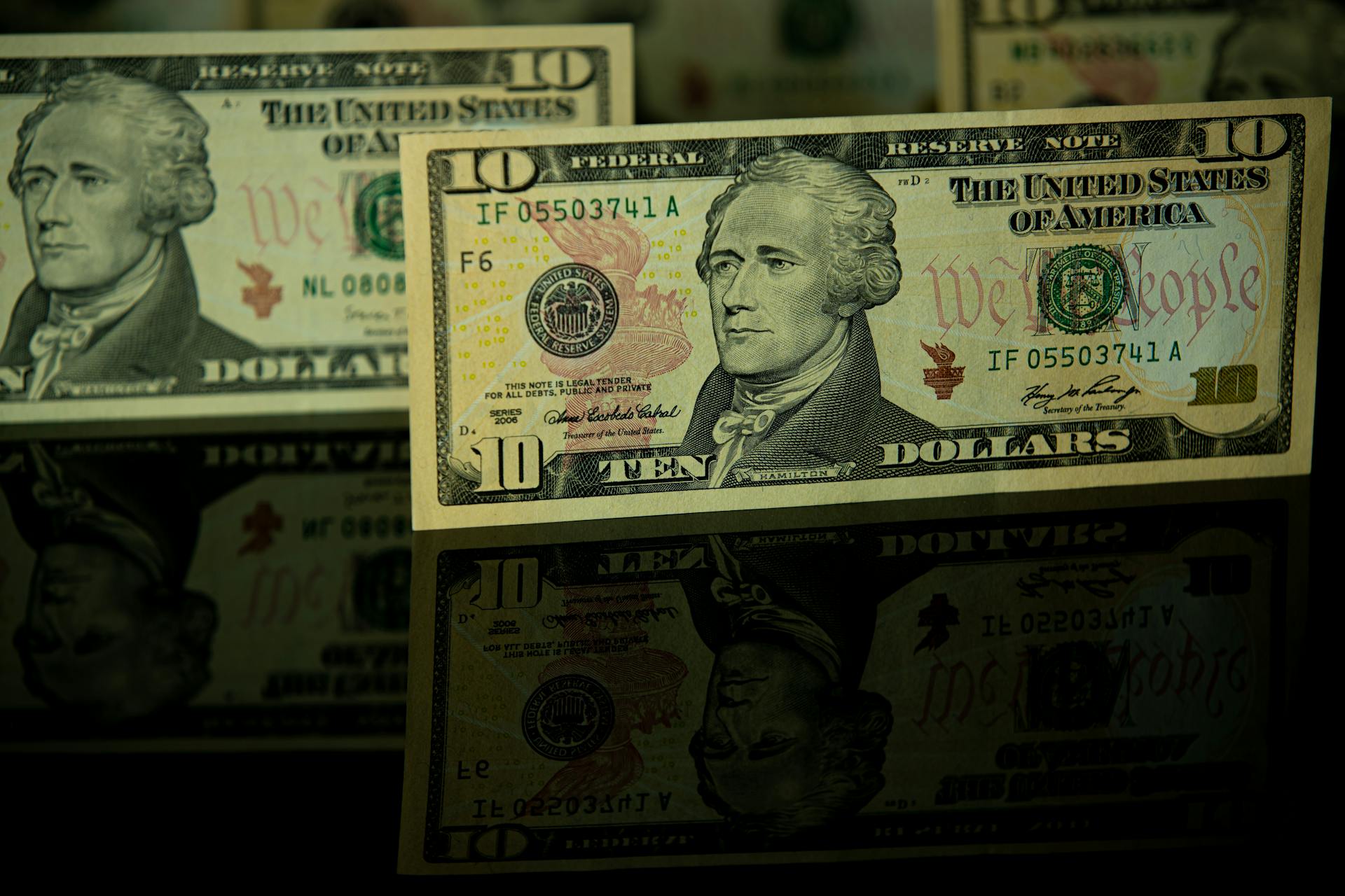 Detailed image of US ten dollar bills displayed with dramatic reflection, highlighting currency design.