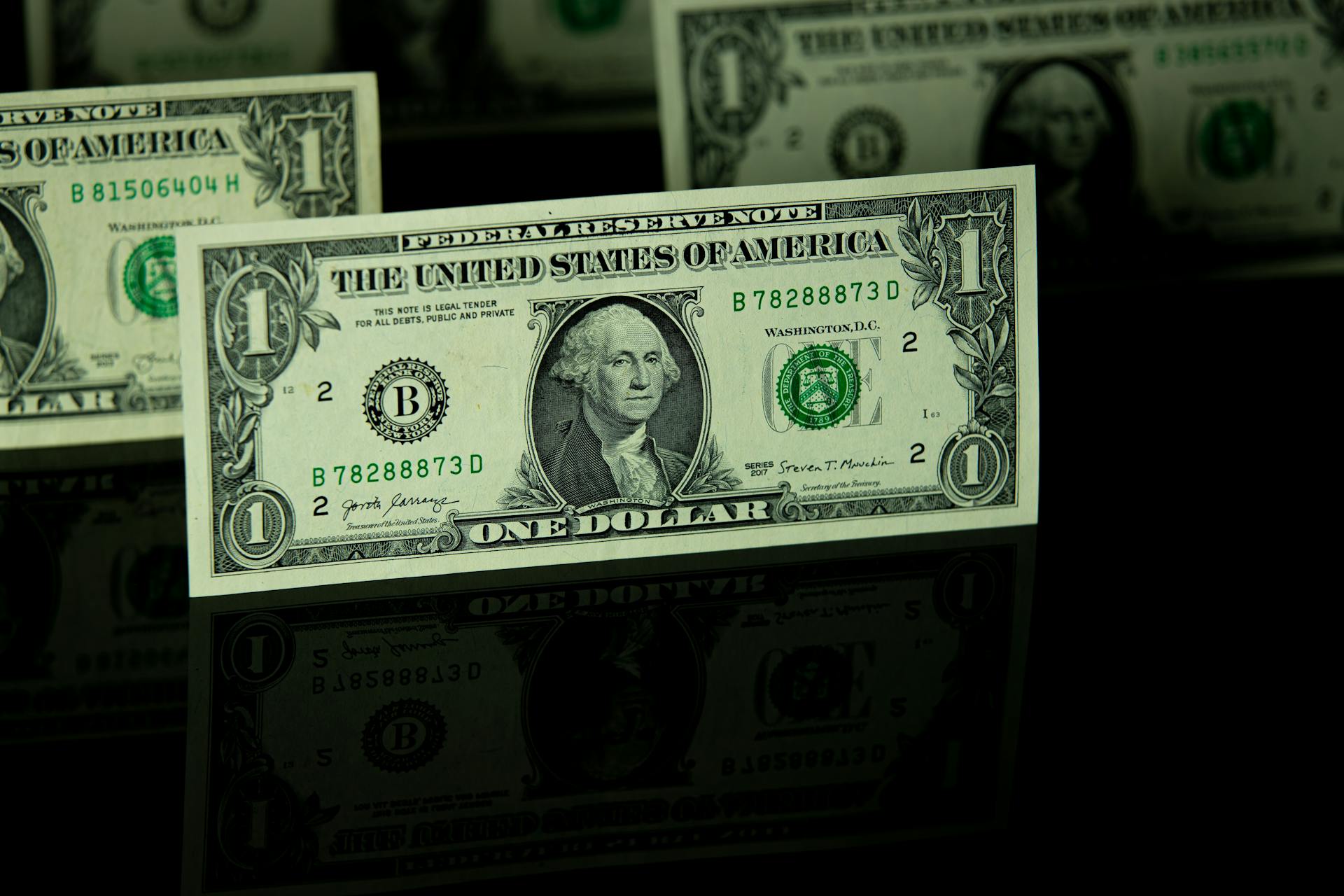 Focused view of US one dollar bills on a reflective black surface.