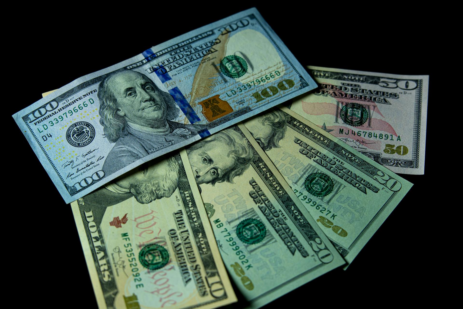 Detailed view of multiple US dollar bills against a black background, highlighting financial themes.