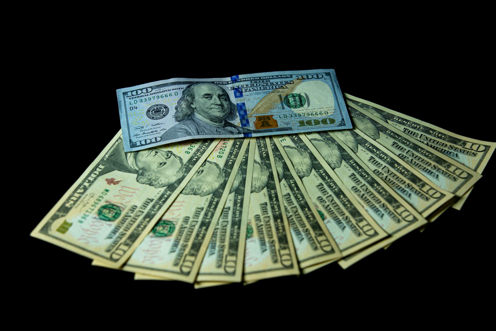 A fanned-out stack of hundred dollar U.S. banknotes on a black background.