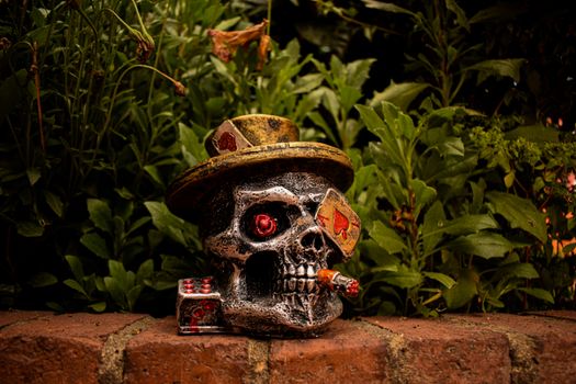 A skull decor with playing cards and cigar set against lush garden greenery.