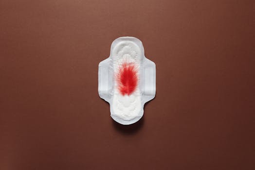 Close-up of a sanitary pad with a red stain on a brown surface, viewed from above.