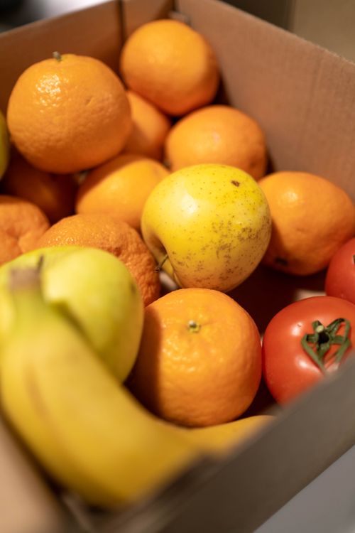 Free Fresh oranges, bananas, apples, and tomatoes artfully arranged in a cardboard box. Stock Photo