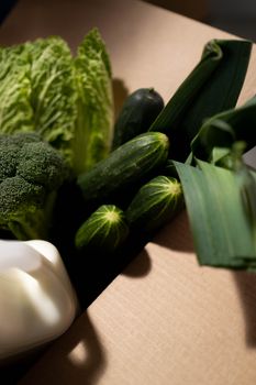 Vibrant green vegetables like cabbage, broccoli, and cucumbers in a cardboard box.