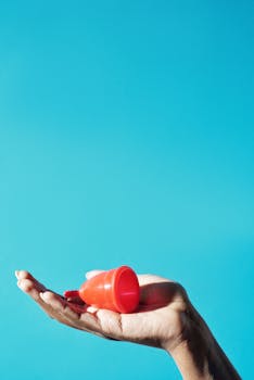 Red menstrual cup displayed on an open hand with a vibrant blue background, highlighting sustainable feminine hygiene.
