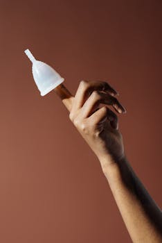 A menstrual cup balanced on a finger against a brown background, symbolizing eco-friendly menstrual care.