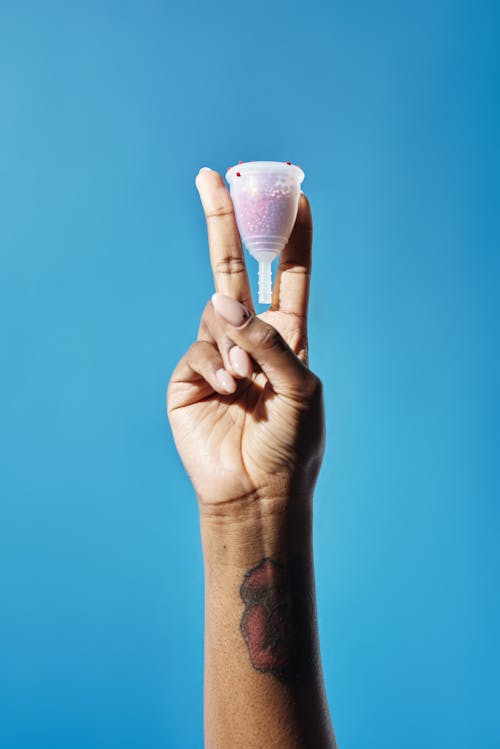 Free A Person Doing Peace Sign while Holding a Full Menstrual Cup Stock Photo