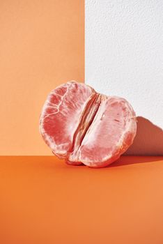 Artistic close-up of a peeled grapefruit against a vibrant orange background, showcasing fresh textures.