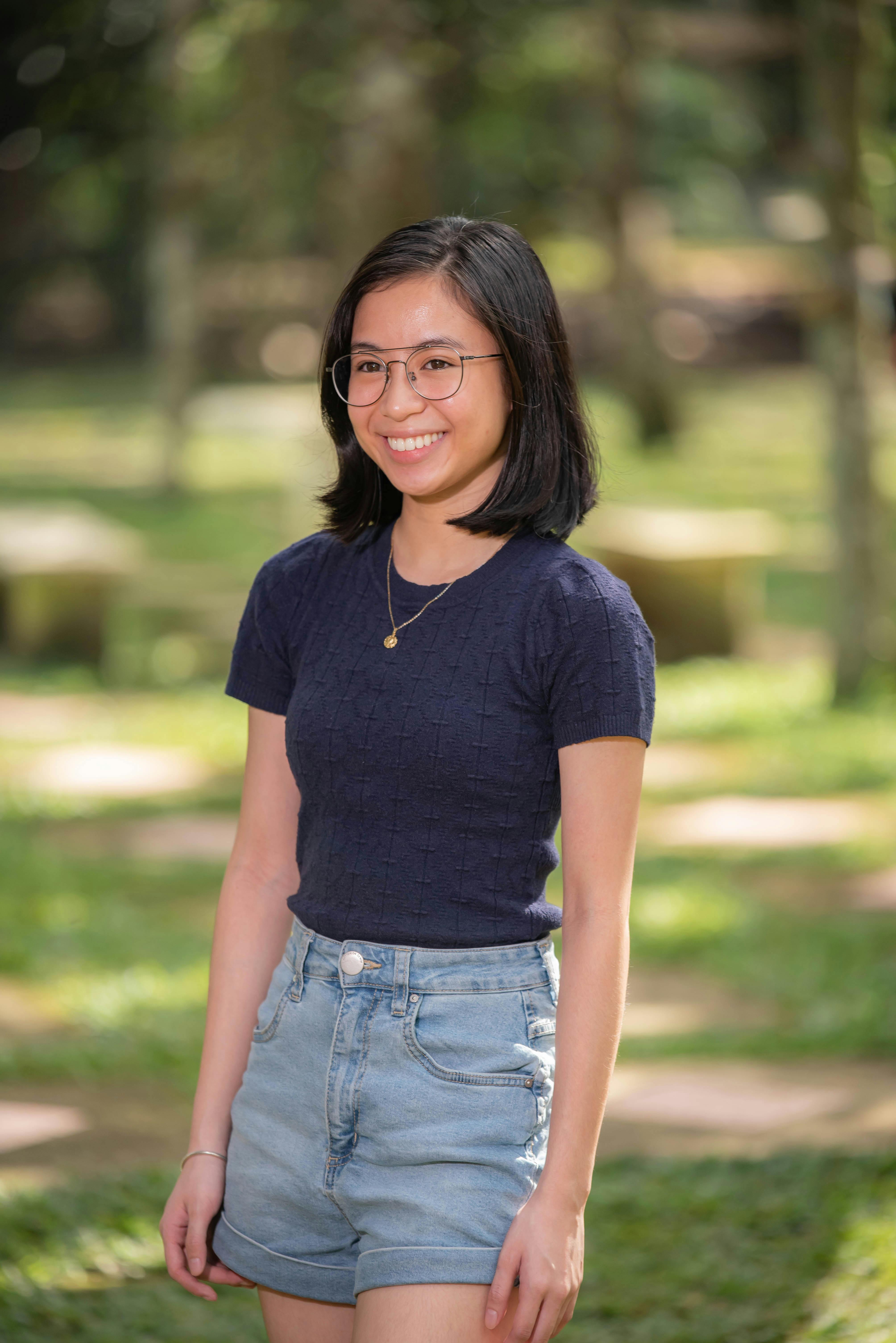 Teenage girl smiling in a sunny park, wearing a casual outfit.