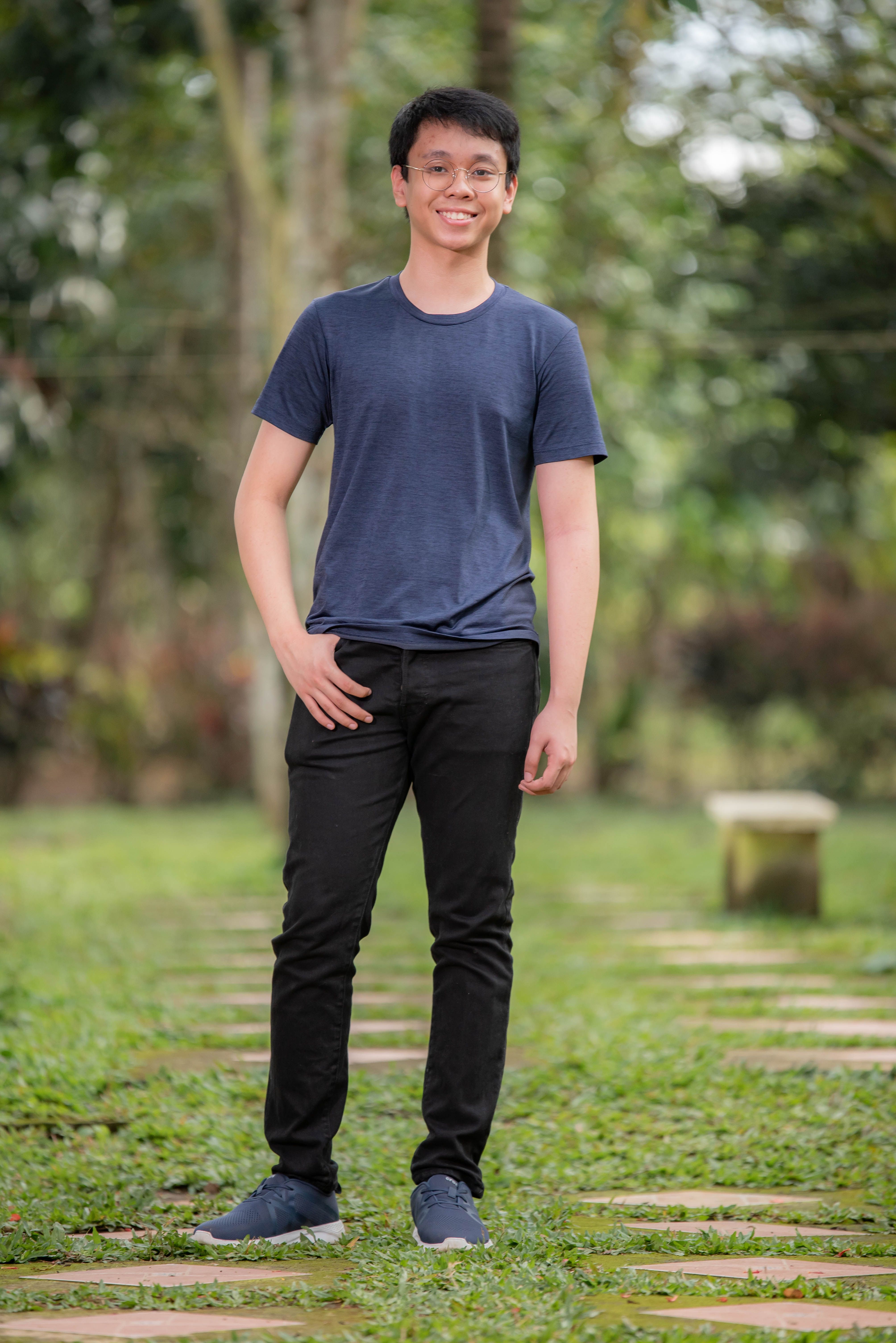 A happy young man wearing glasses standing outdoors in a green park setting.