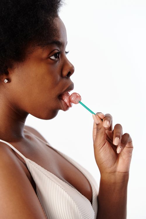 Free Side view of an African American woman licking a lollipop in a studio setting. Stock Photo
