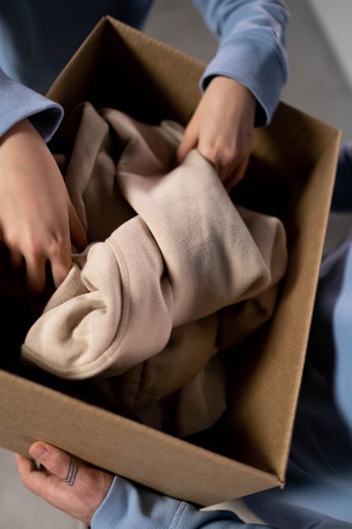 Free Close-up of hands sorting clothes into a cardboard box for charity donations. Stock Photo