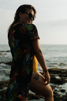 Cheerful female with stylish tattoo smiling and resting on coast with stones near rippling sea