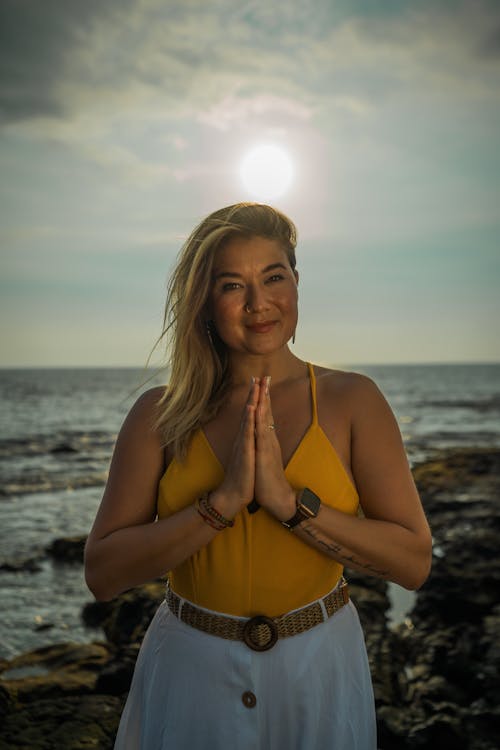 Tranquil female smiling and looking at camera while practicing surya namaskar asana on shore near rippling sea in tropical resort