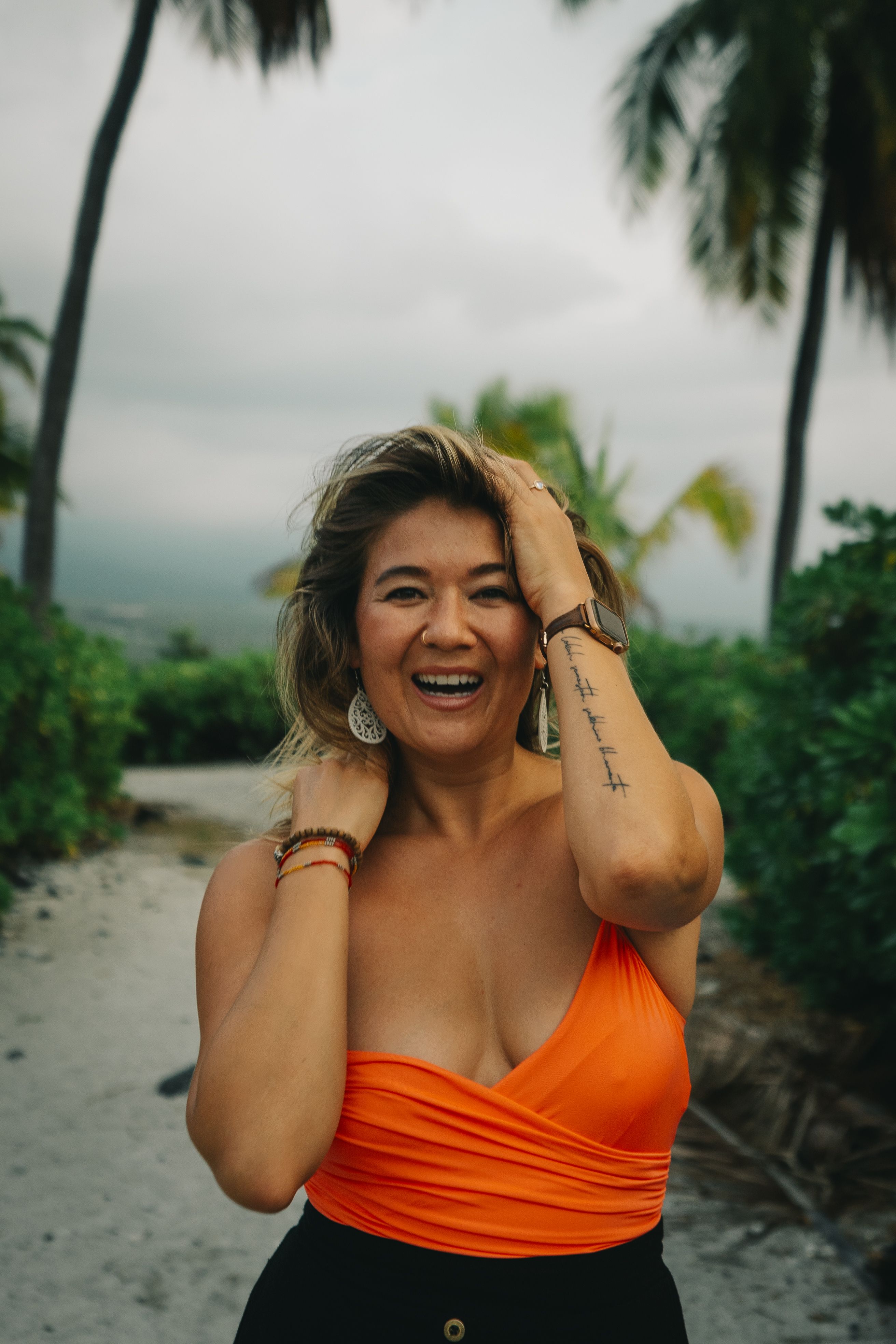 Joyful woman in orange top enjoying a tropical beach day, surrounded by palm trees.