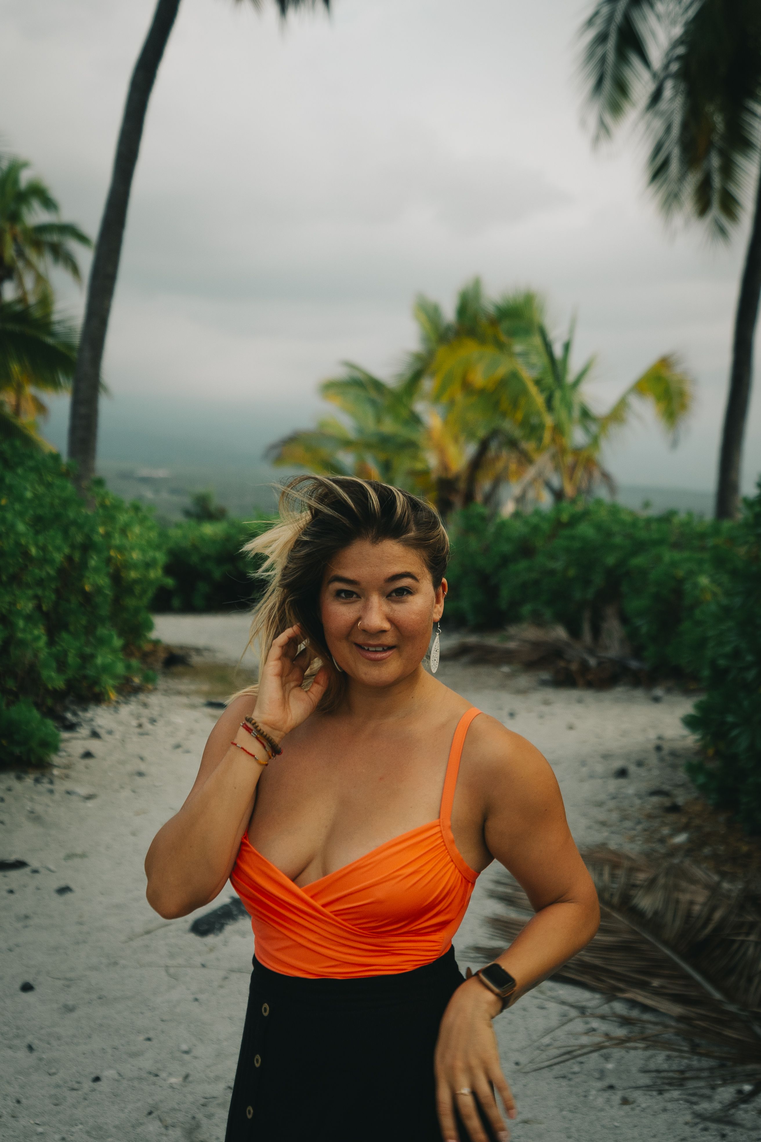Portrait of a woman standing on a tropical beach path with palm trees in the background.