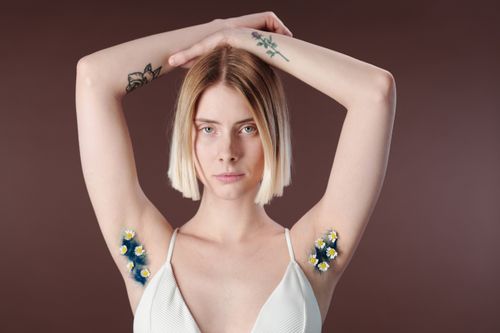 Free Portrait of a young woman with tattoos and floral designs, arms raised. Stock Photo
