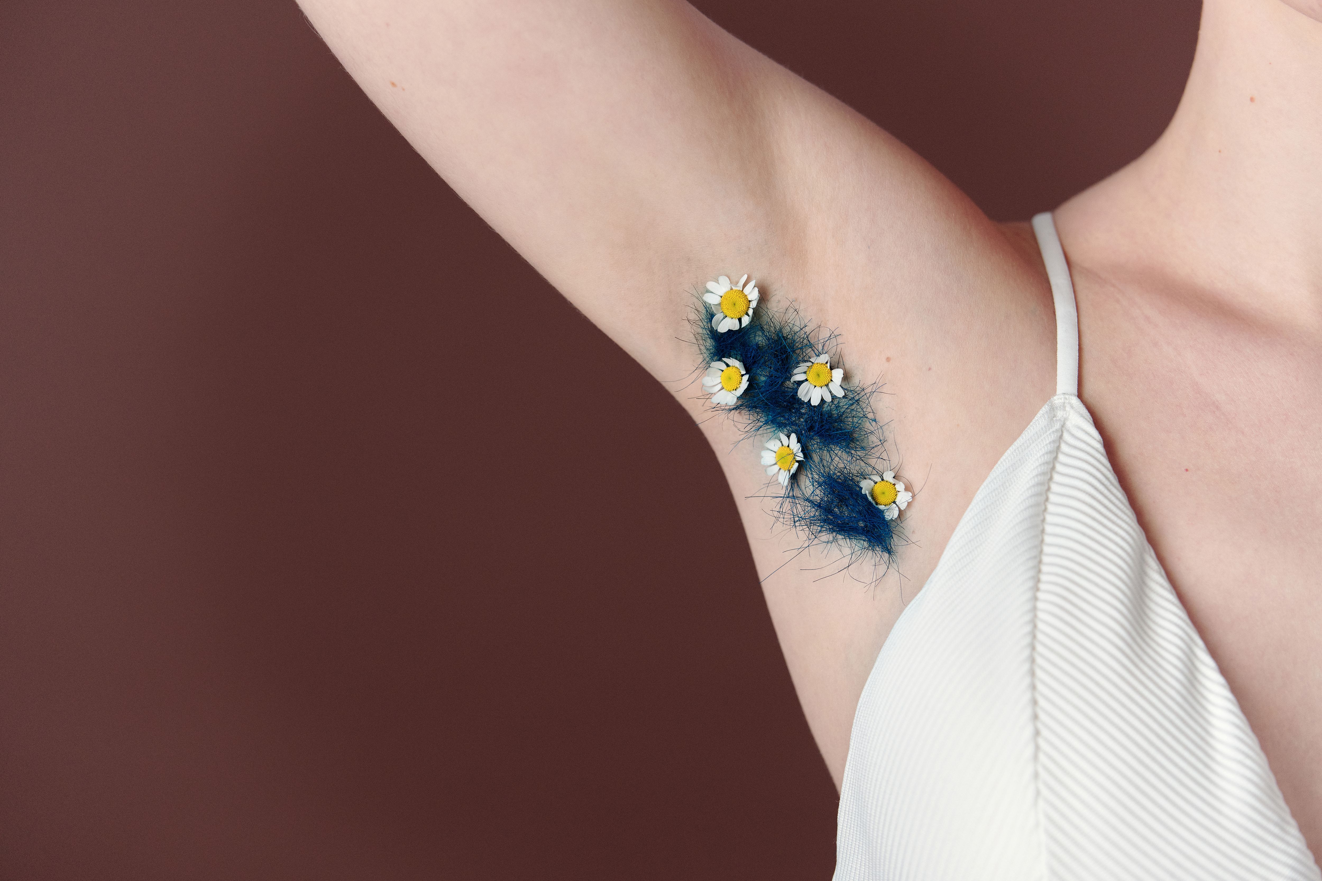 A unique artistic close-up of underarm hair decorated with daisies against a brown background.