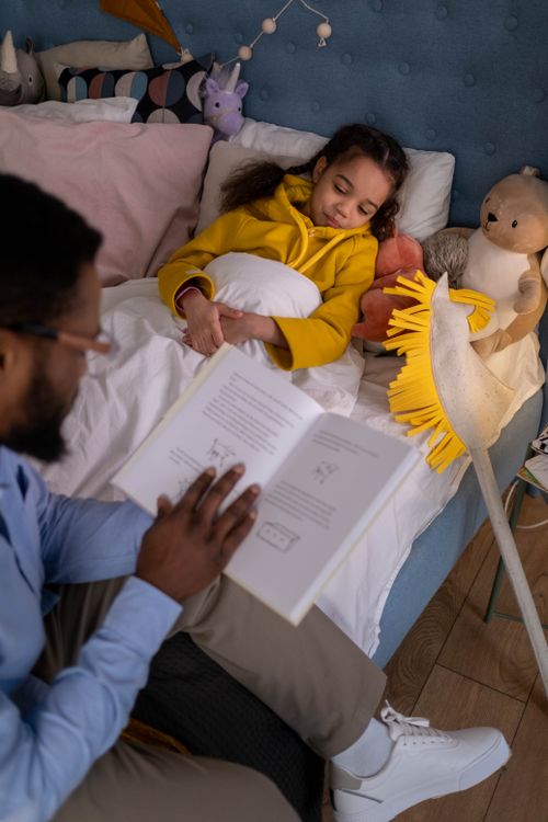 Free A father reading a bedtime story to his daughter tucked in bed with her stuffed toys. Stock Photo
