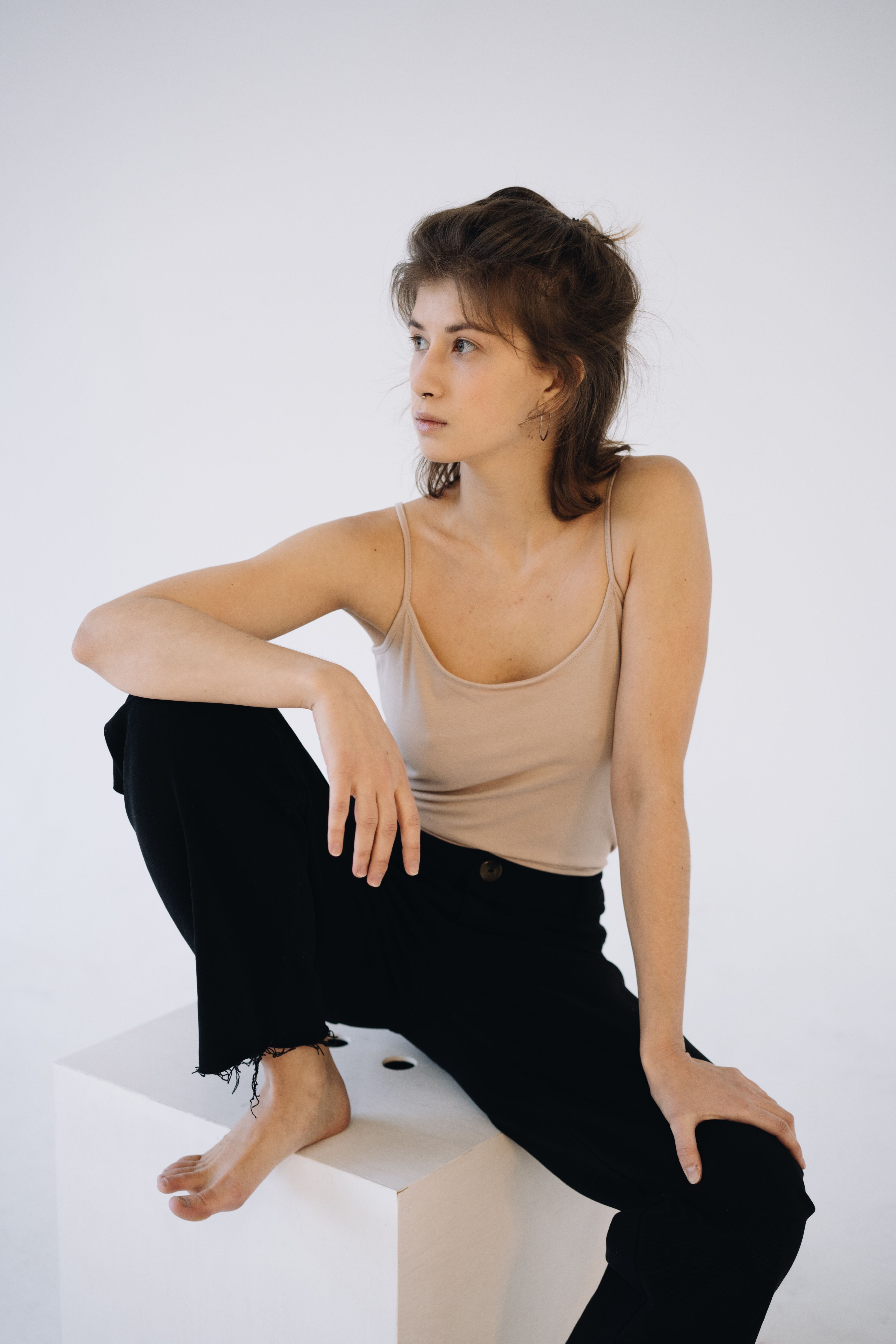 Elegant portrait of a woman sitting on a white platform in a studio setting.