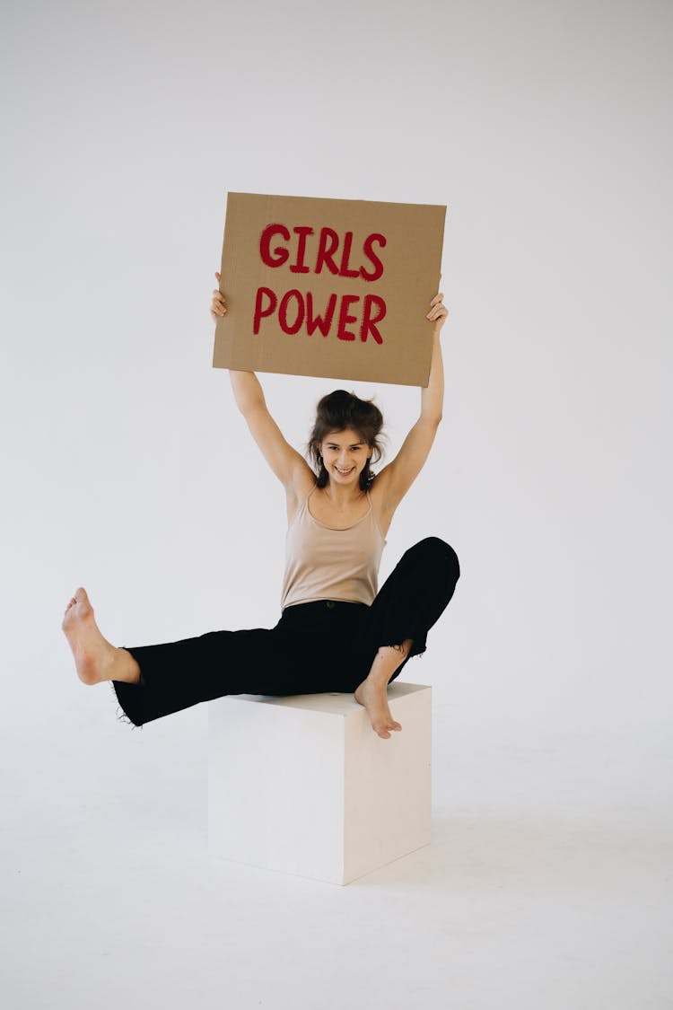 A Woman Sitting On White Platform While Holding A Placard