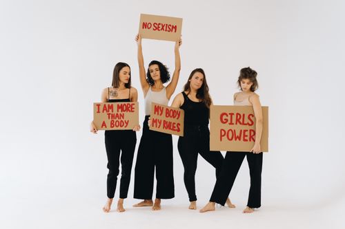 Free A group of diverse women holding feminist signs advocating for equality and empowerment against a plain backdrop. Stock Photo