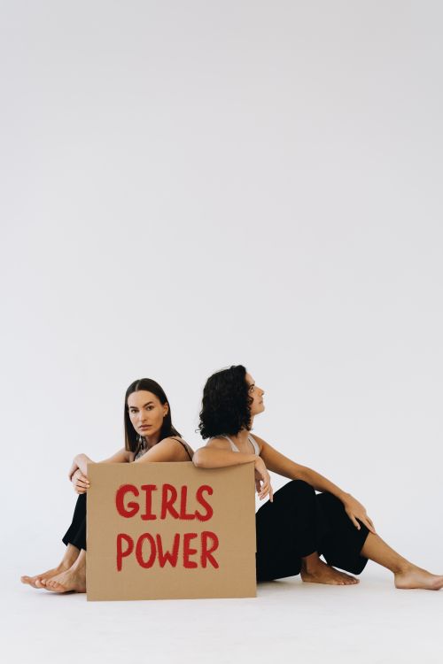 Free Two women sit back-to-back holding a 'Girls Power' sign, symbolizing empowerment. Stock Photo