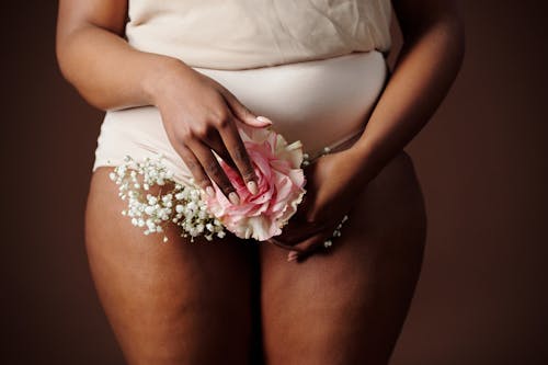 Free Hand Holding Flowers in Front of Lower Abdomen Stock Photo