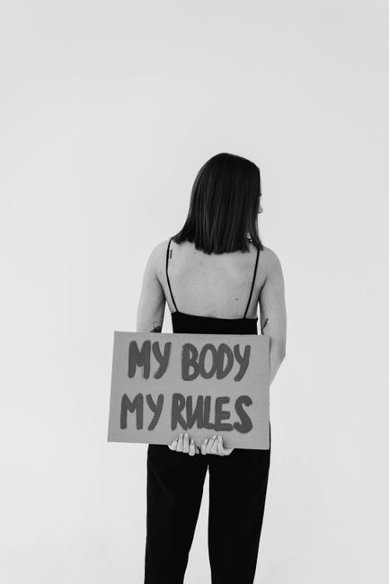 Back view of woman holding a 'My body my rules' sign, promoting empowerment.