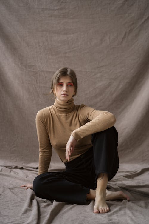 Woman in Brown Turtleneck Long Sleeves Shirt and Black Pants Sitting on the Floor while Looking Afar