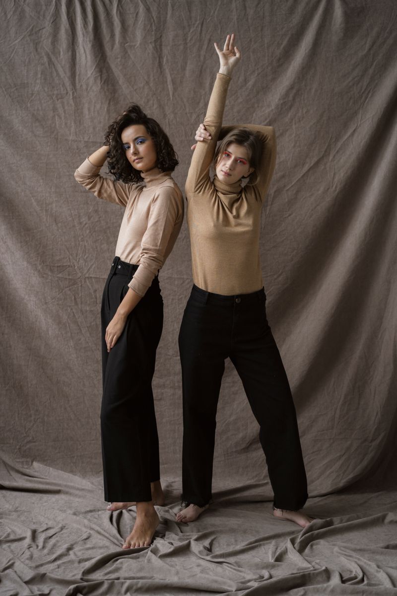 Two models in neutral knit tops and black trousers