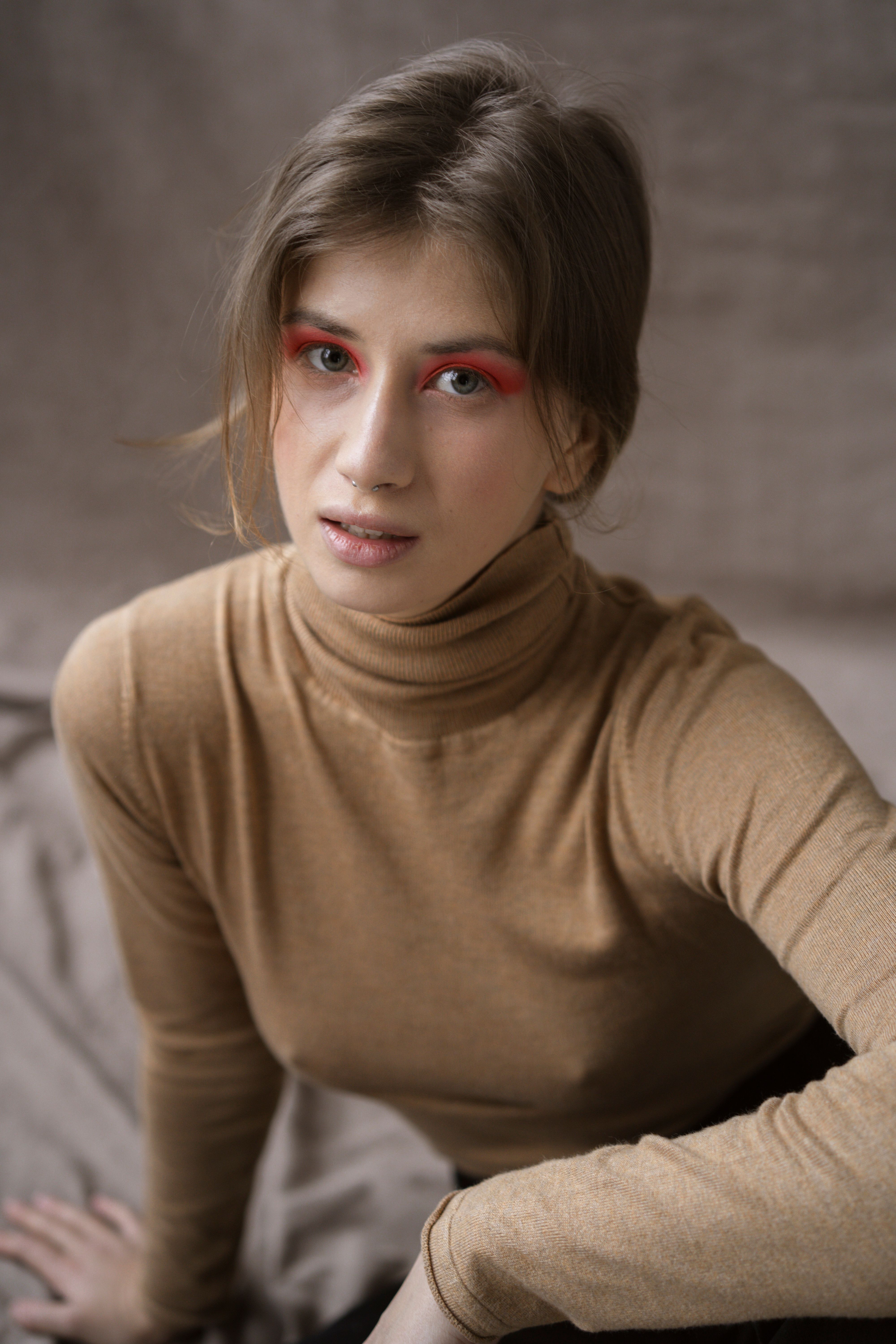 Close-up portrait of a woman in a brown turtleneck with artistic eye makeup.