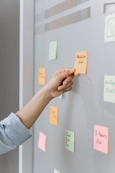 A hand placing colorful sticky notes on a glass wall, ideal for brainstorming and office planning visuals.