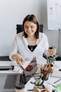 Smiling woman in an office working at her desk with a laptop and coffee.
