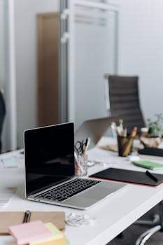 A neat office desk setup with an open laptop, stationery, and plant, ideal for business or remote work themes.