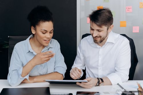 Free Two professionals discussing ideas in an office setting with documents and a digital tablet. Stock Photo