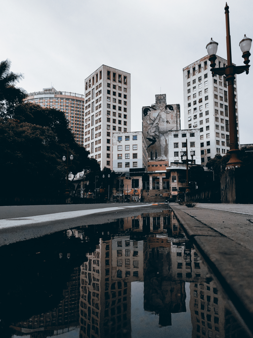 Free Captivating urban cityscape featuring tall buildings and a striking reflection in a puddle, creating a dramatic effect. Stock Photo